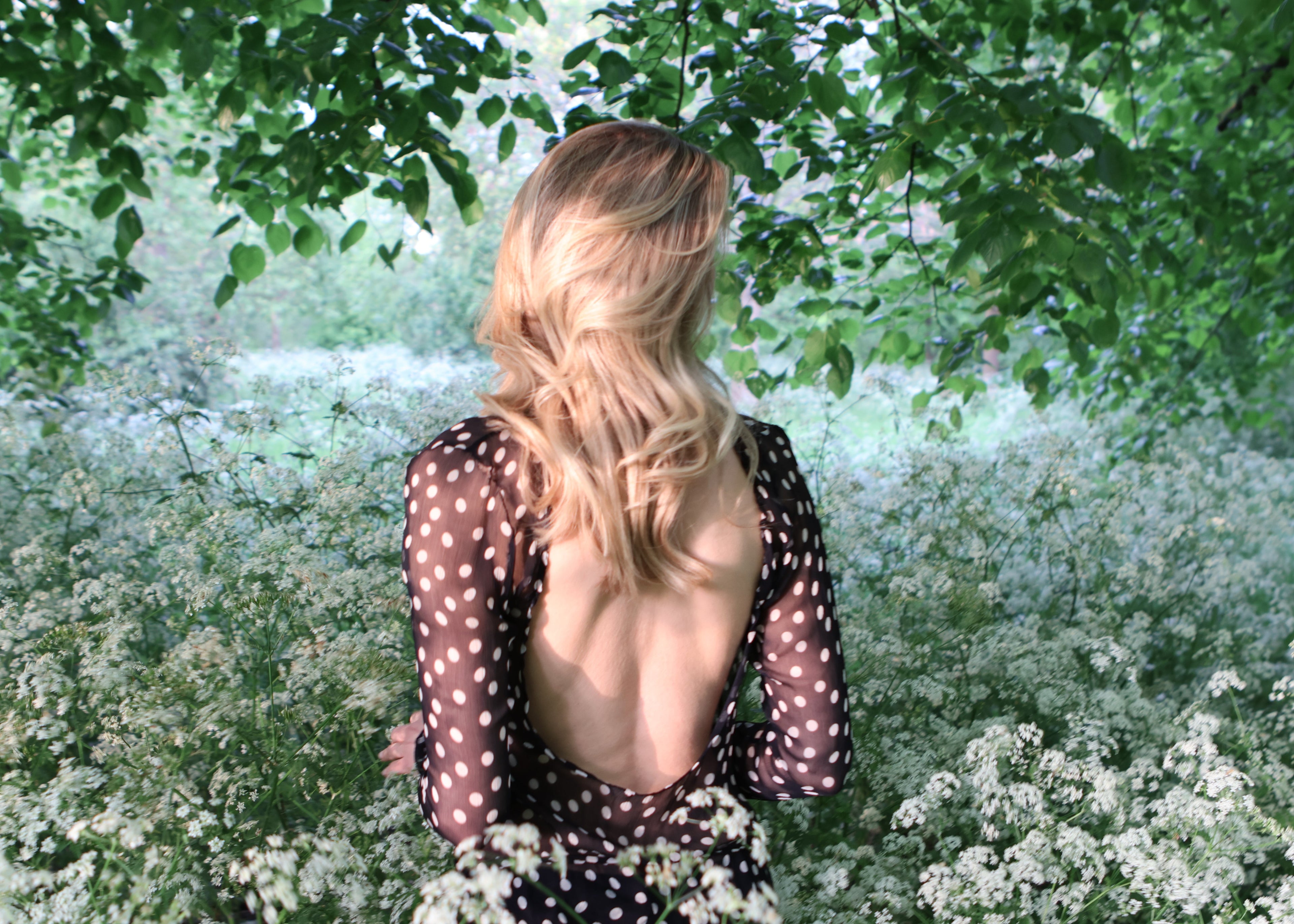 Woman in a polka dot dress standing among white flowers and greenery